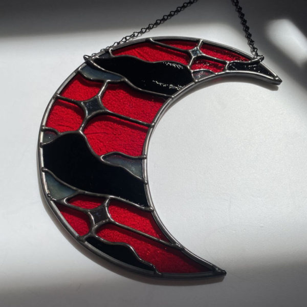 Red and black stained glass cloudy moon suncatcher laying on white floor