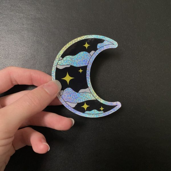 Glittery iridescent moon sticker being held.